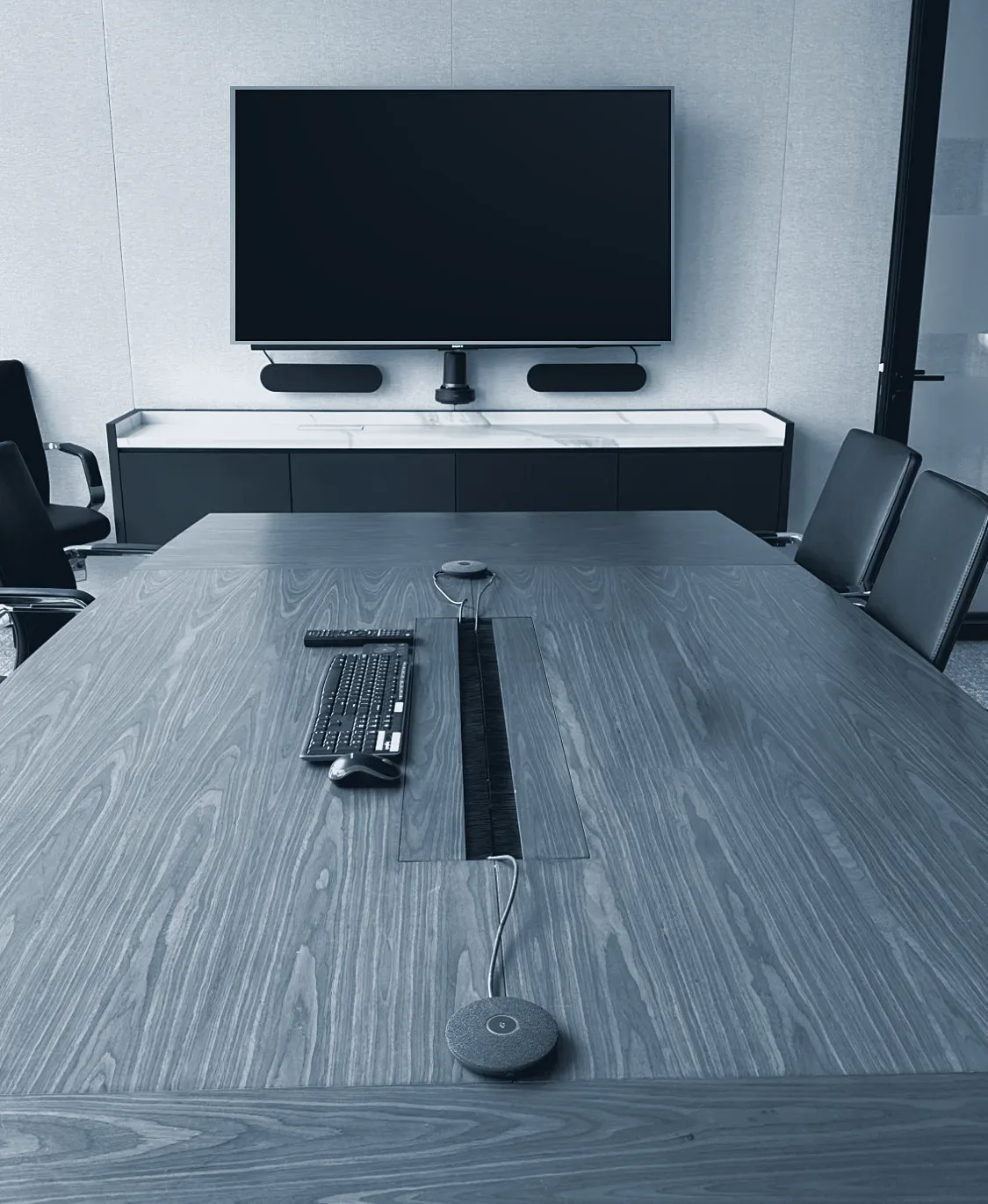 A boardroom with a wall screen, camera and table microphones