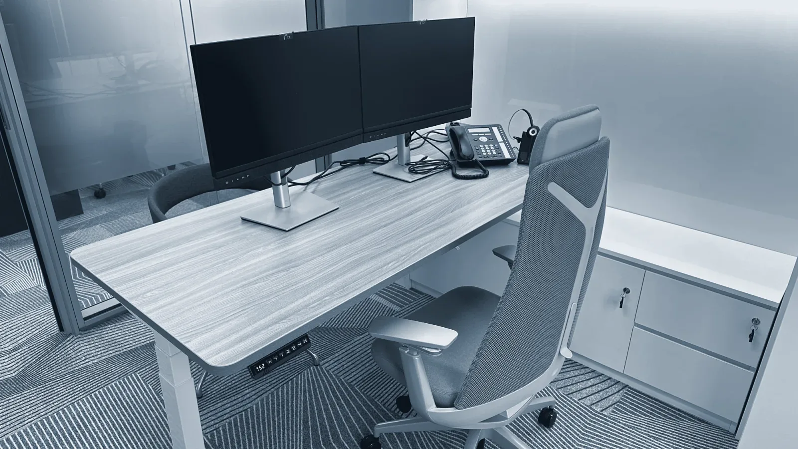 A desk with two screens, a desk phone and a wireless headset