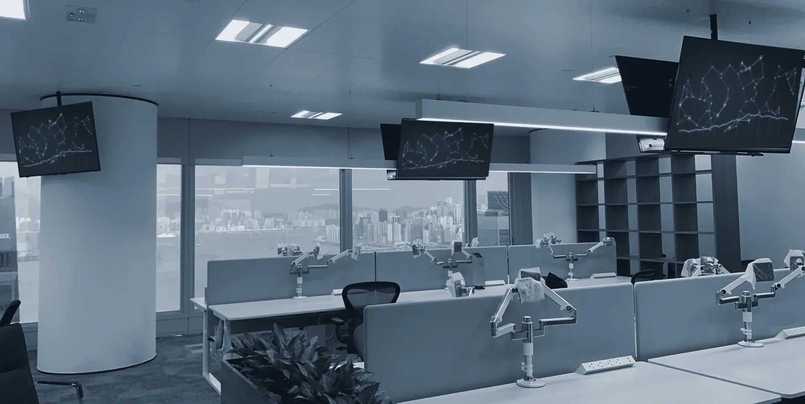 Desks with monitor arms and wall screens on an office floor